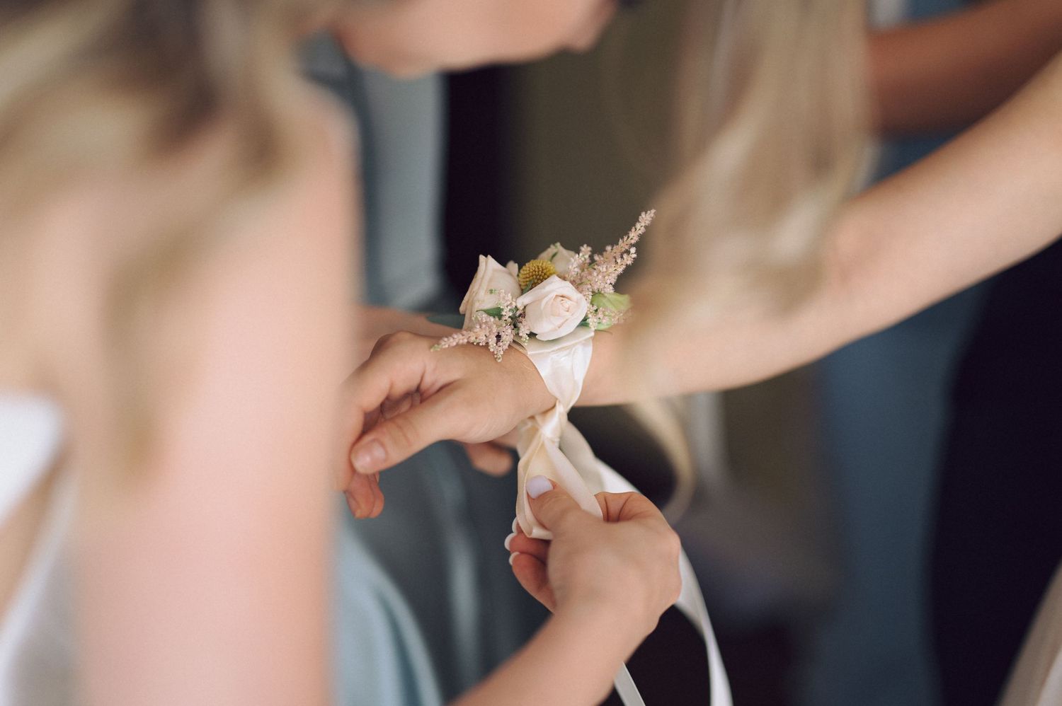Someone secures a delicate floral wrist corsage with white blooms for a formal occasion.