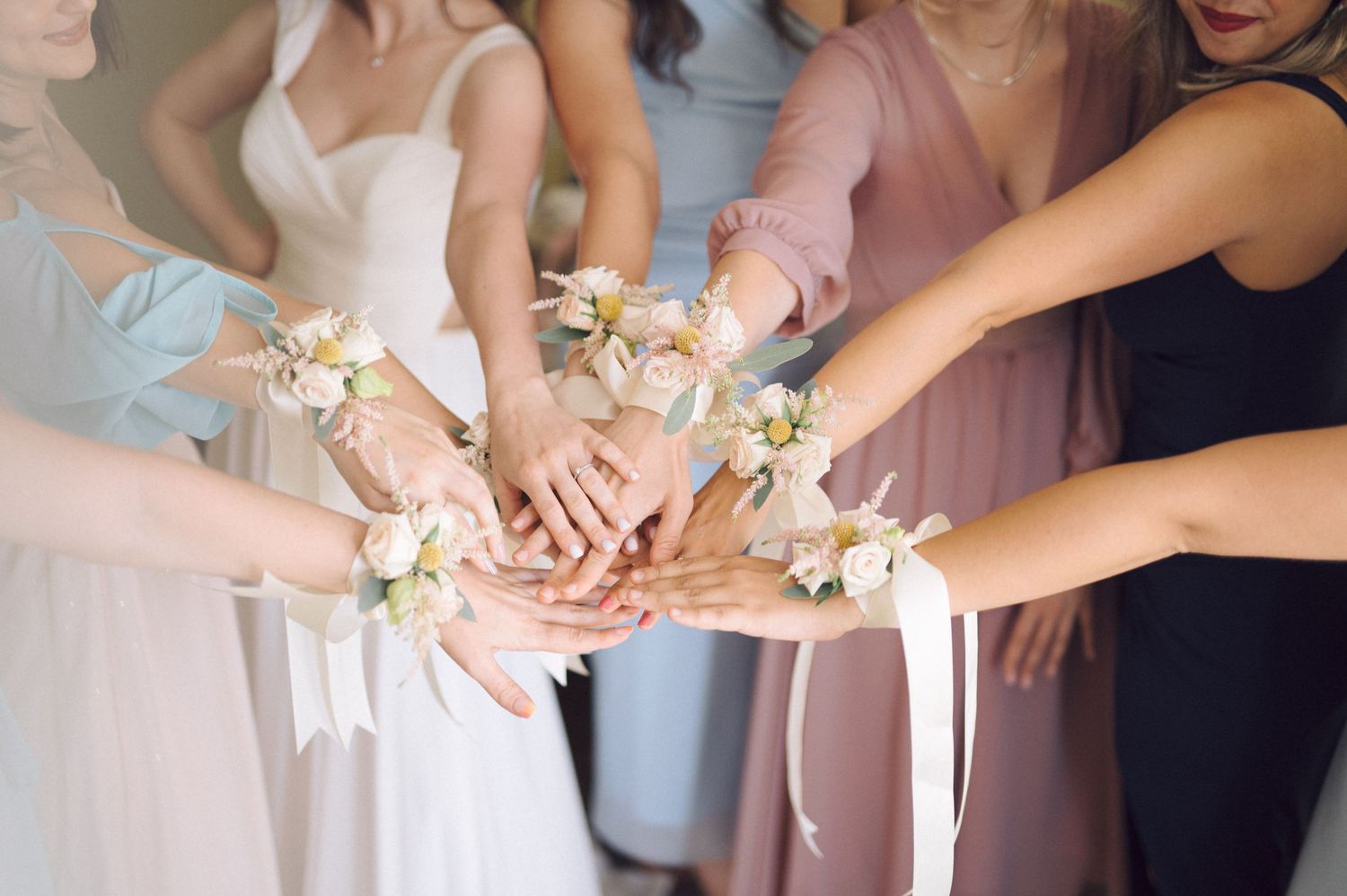 Five hands reach together in coordinated pose wearing matching pink floral corsages on their wrists.