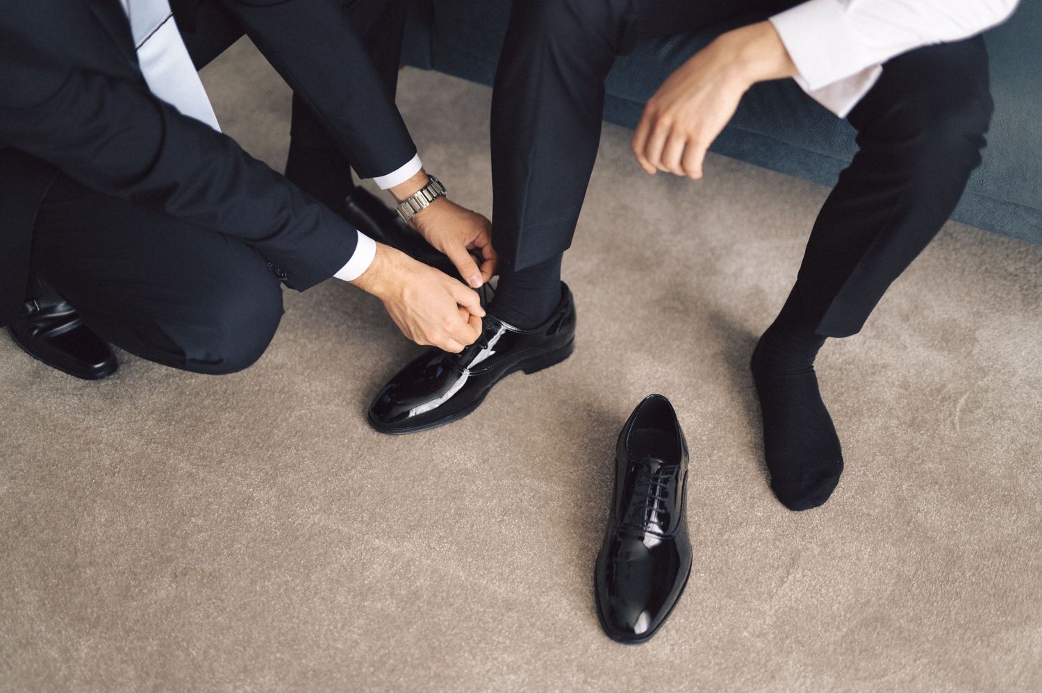 Four pairs of formal black shoes shown at floor level, worn by people in black pants at what appears to be a business event.