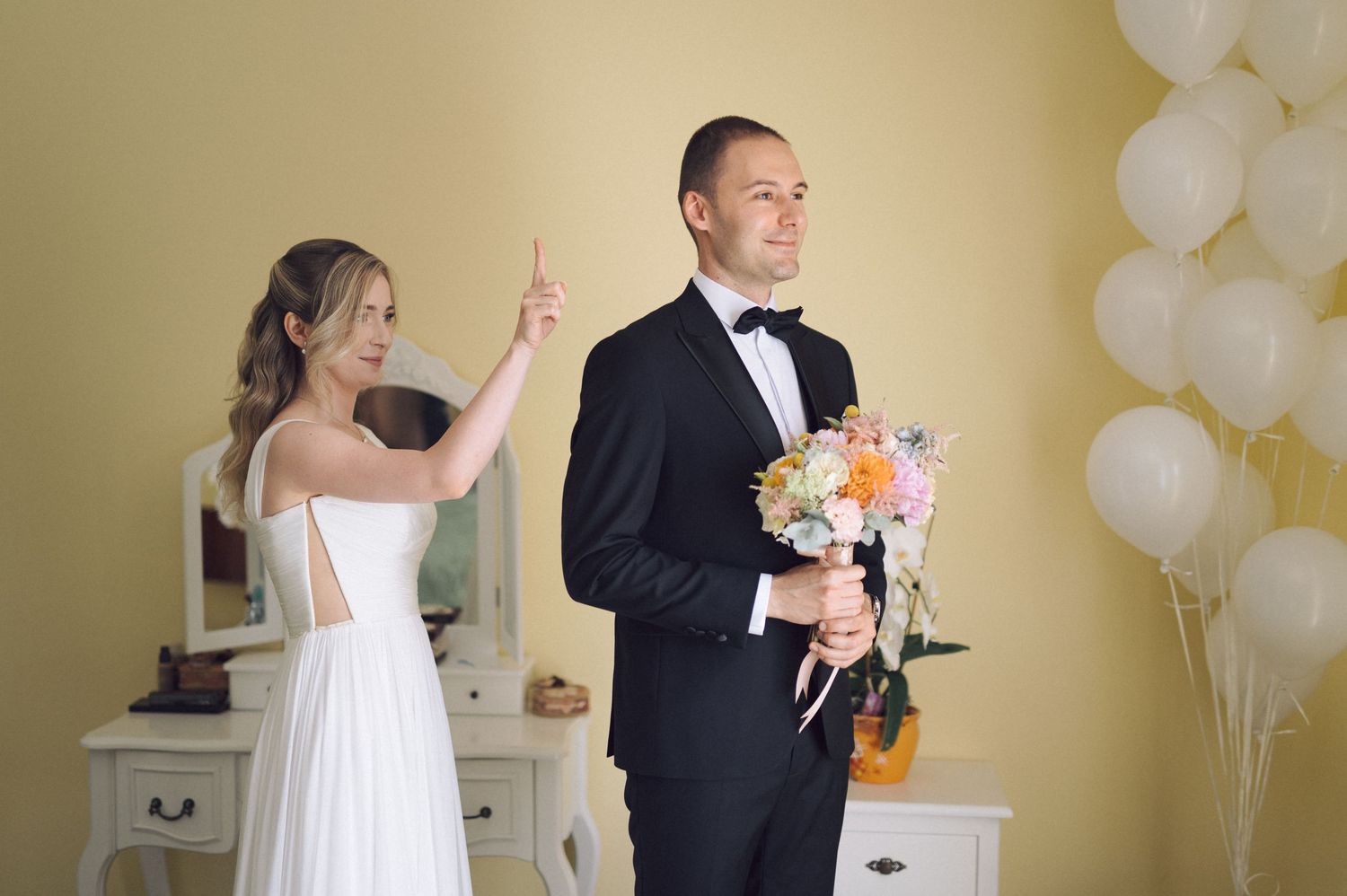 A couple shares a first look moment before their wedding with white balloons and floral bouquet nearby.