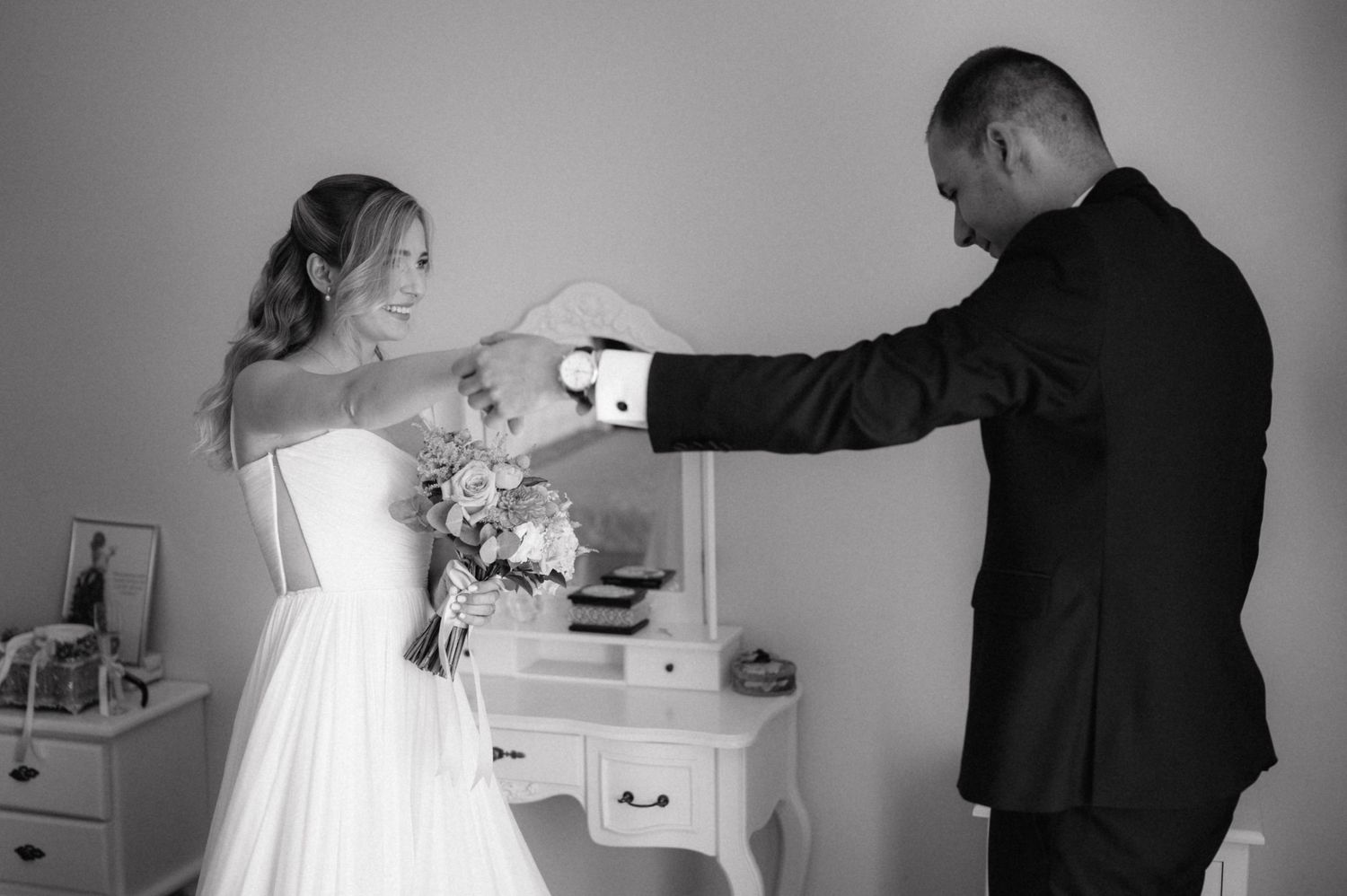 A cinematic black and white photo sequence shows a couple in formal wedding attire sharing tender moments in a kitchen.