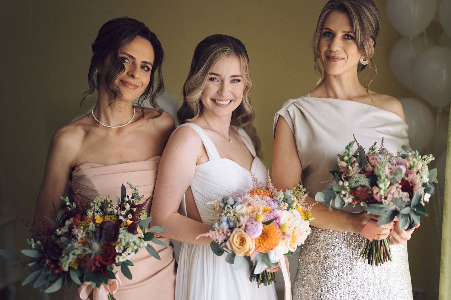 Bridesmaids in pastel dresses hold beautiful bouquets while sharing joyful laughter during wedding party photos.