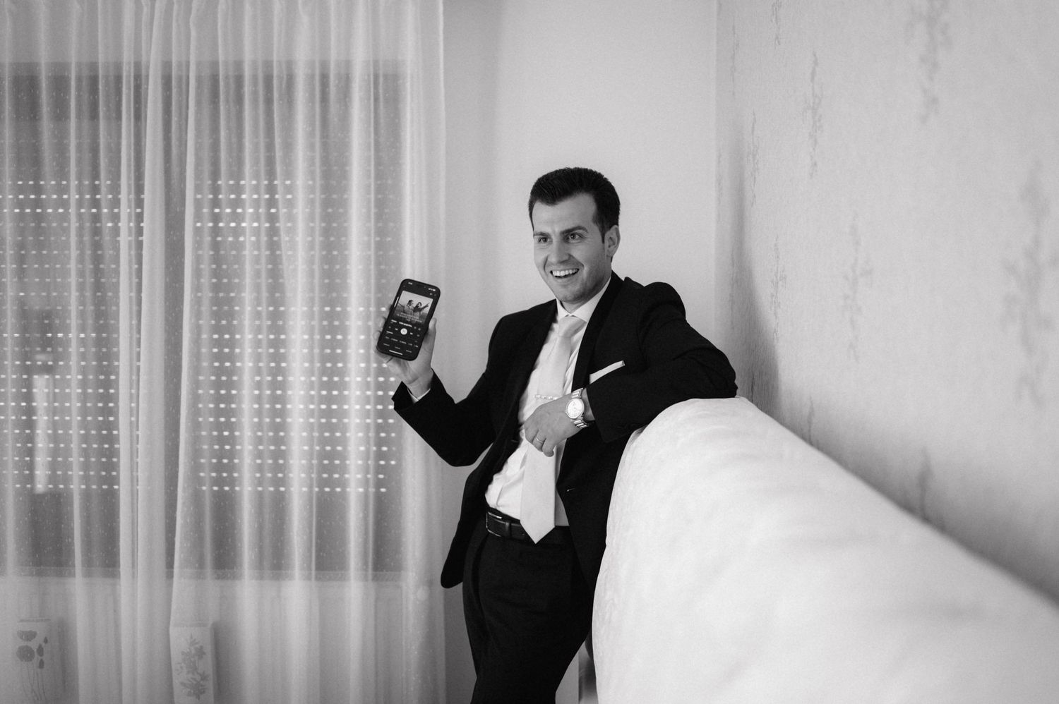 Black and white photo of someone in a suit holding a mobile phone while leaning against a wall.