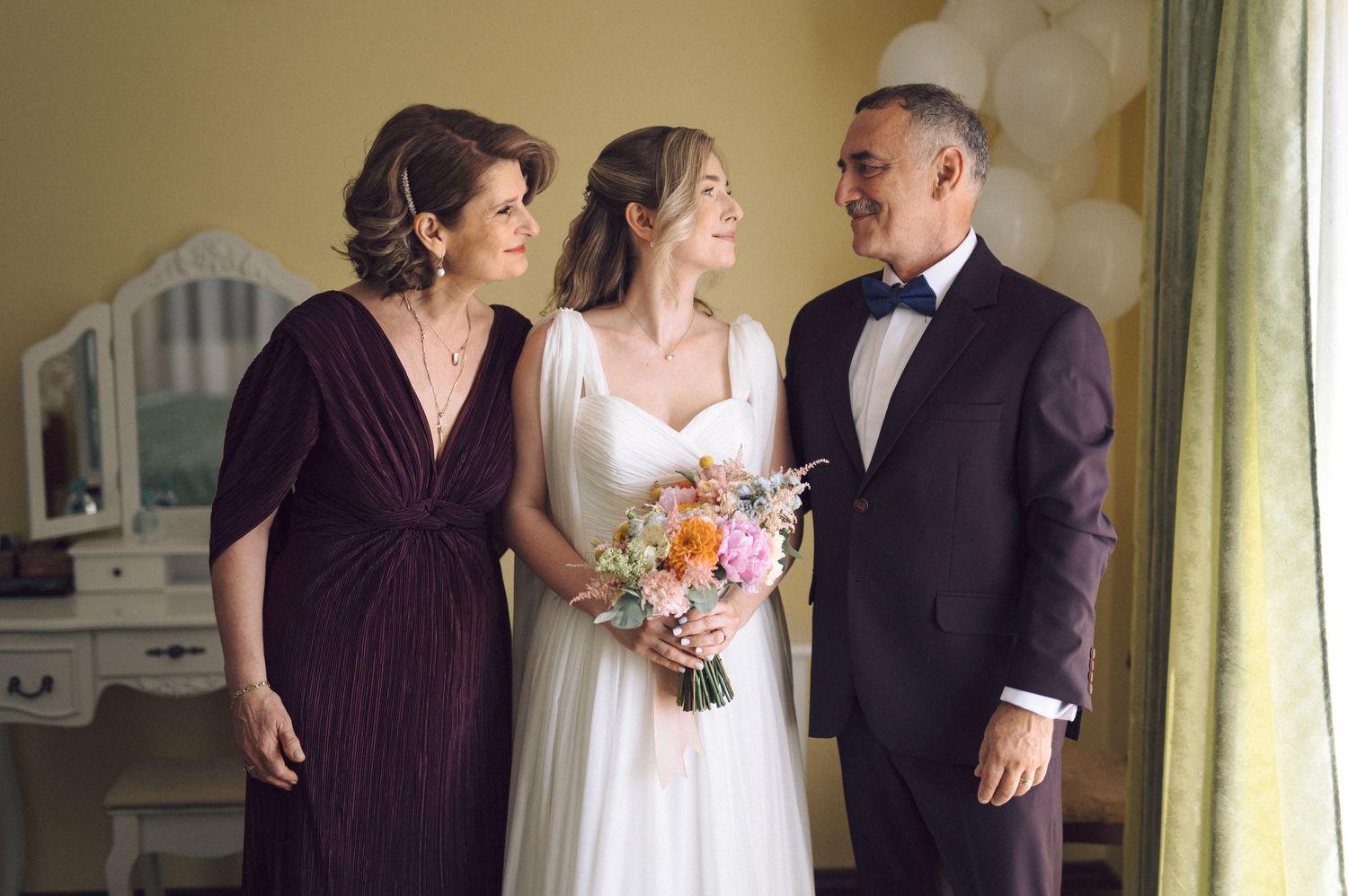 Wedding party members share tender moments during pre-ceremony preparations in a sunlit room.