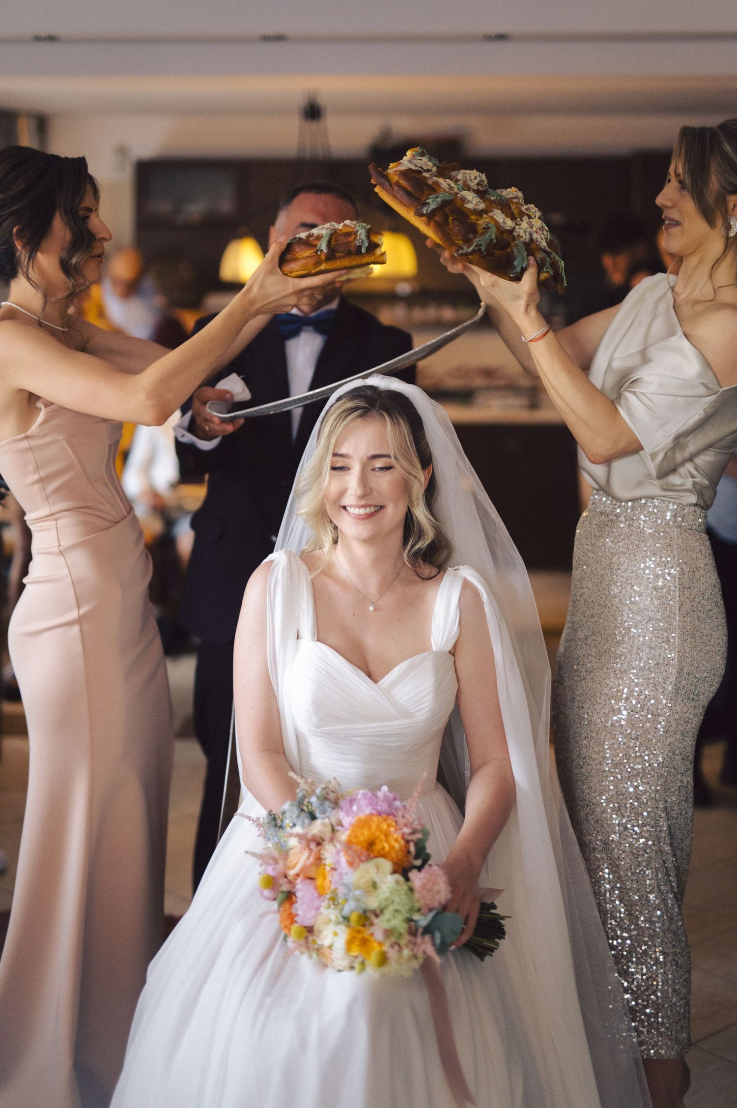 Wedding party in blush pink and silver sequin dresses dances beside a bride in a white gown holding a vibrant bouquet.