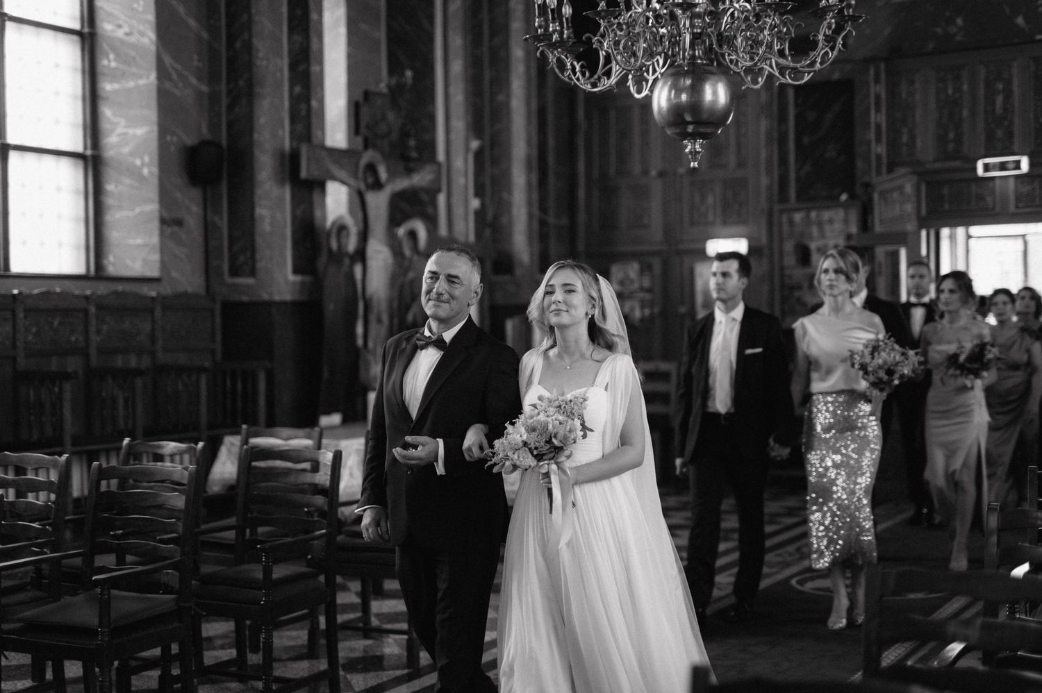 A series of black and white wedding ceremony photos showing candid moments in a dimly lit church with chandelier lighting.