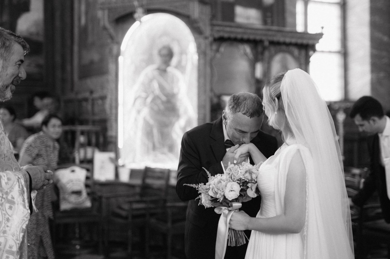 A black and white photograph of a wedding ceremony taking place inside a church with a statue visible in a niche.