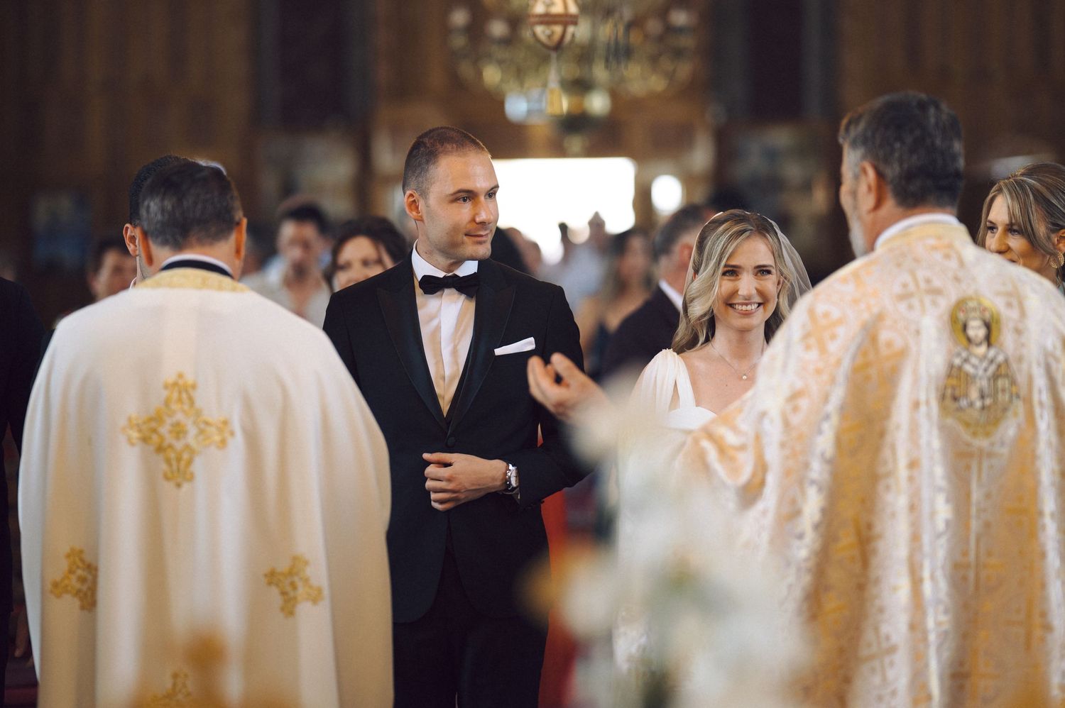 Couple stands with clergy members wearing ornate robes during traditional church wedding ceremony.
