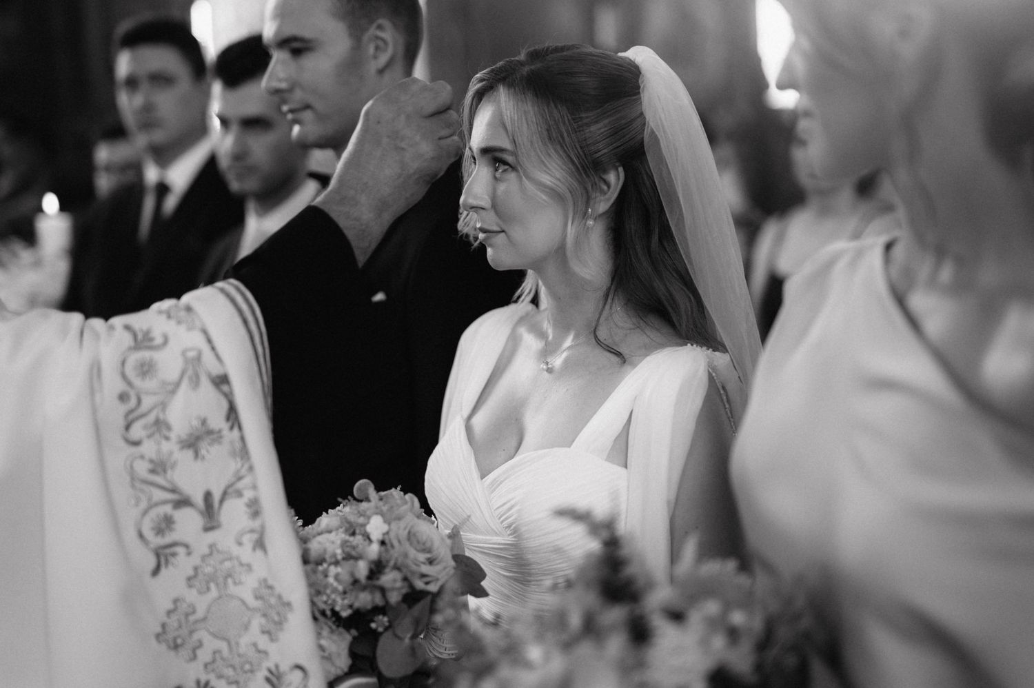 Black and white photo of a bride in a white dress holding a floral bouquet during a wedding ceremony.