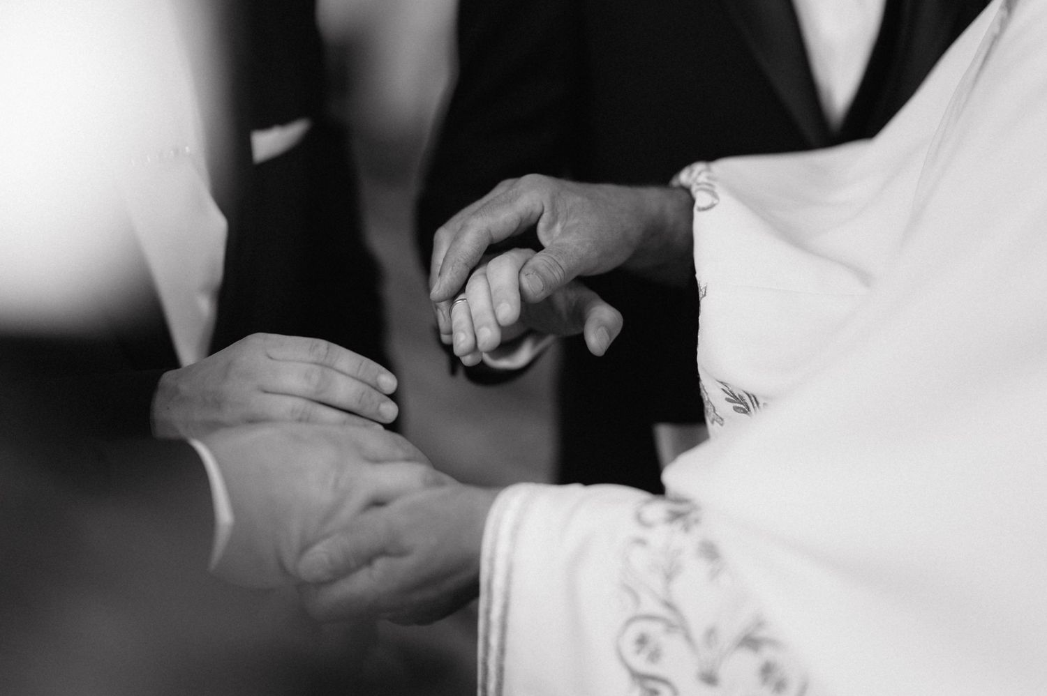 Close-up black and white photo of hands clasped together during a wedding ceremony.
