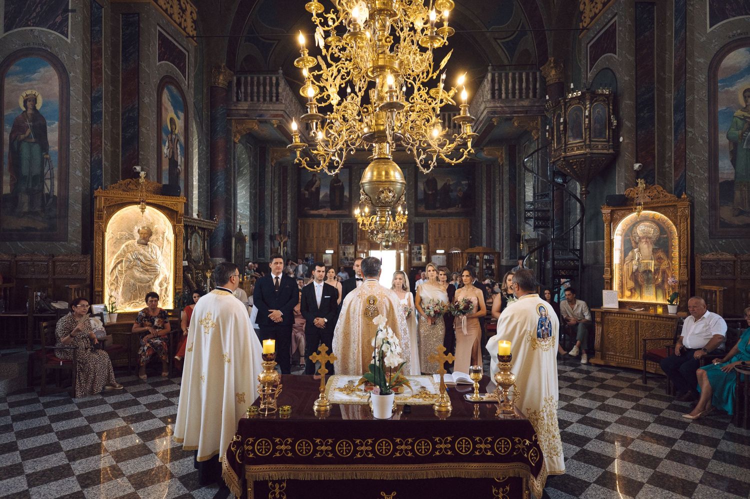 Religious ceremony taking place in an ornate cathedral with golden chandelier and decorative interior architecture.