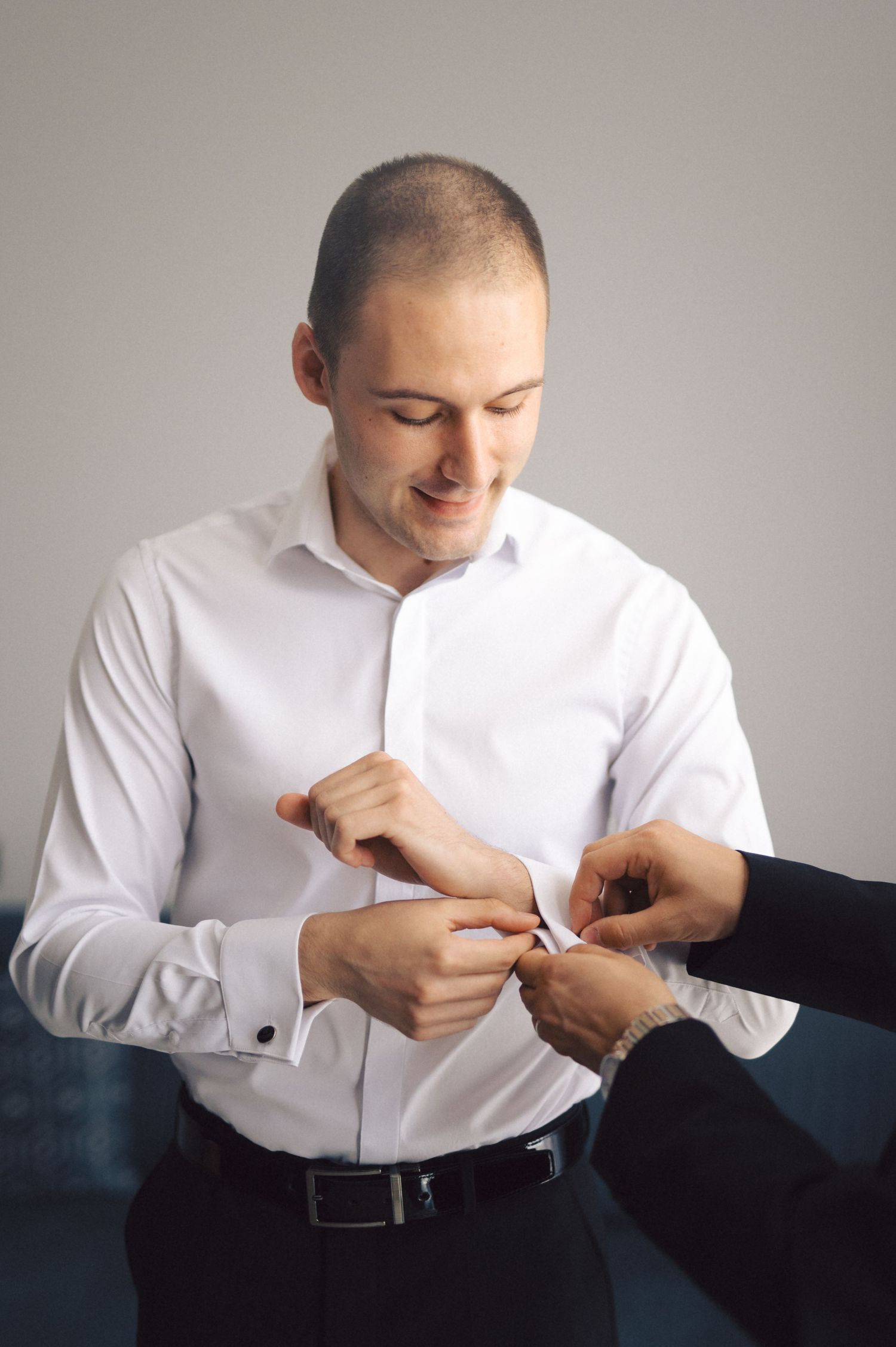 Someone wearing a white dress shirt is getting help fastening cufflinks before a formal event.