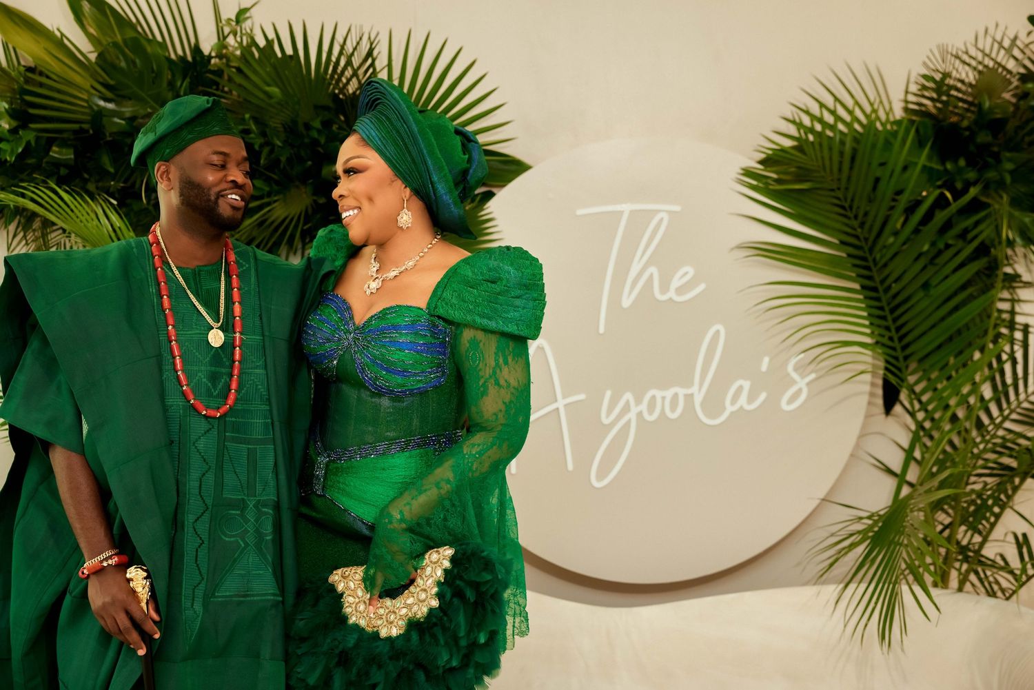 Couple in matching green traditional Nigerian attire posing against tropical backdrop.