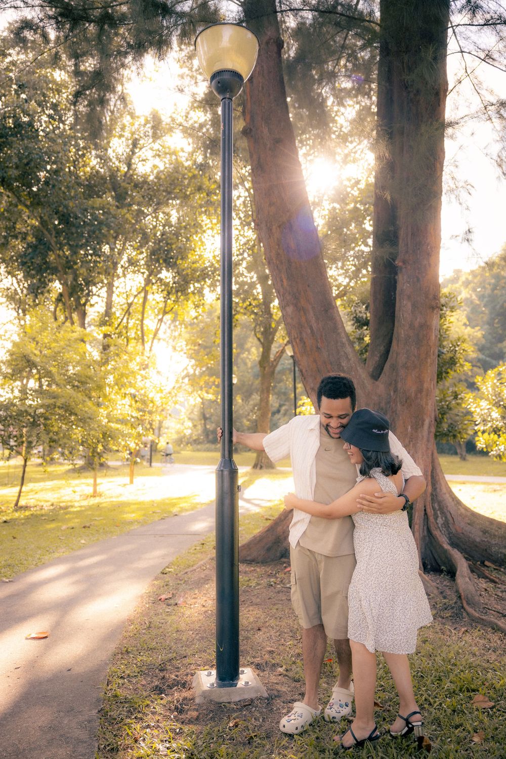Romantic couple walks along a sunlit park path with golden sunlight filtering through autumn trees.