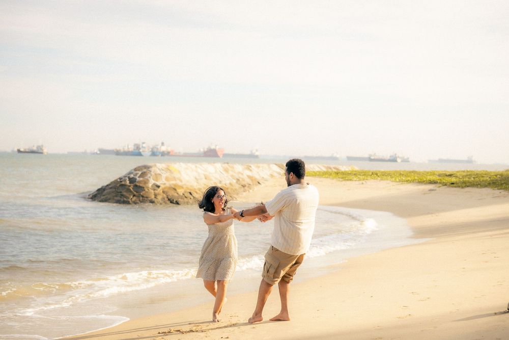A couple in white outfits walks along a serene beach shoreline during sunset.