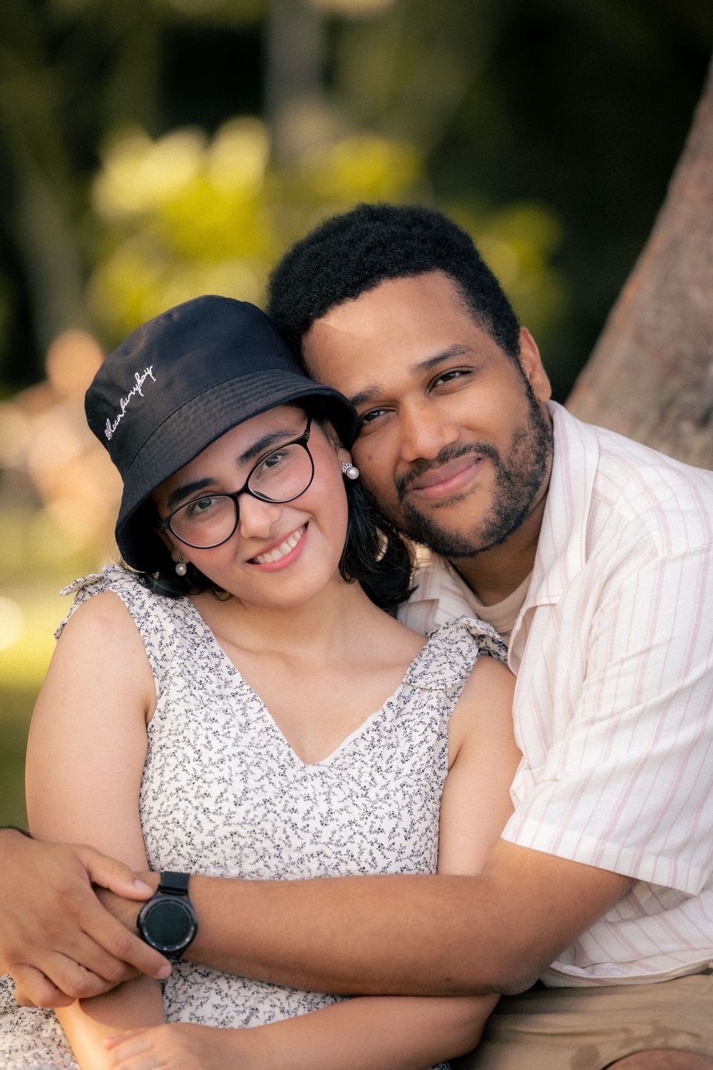 A couple in matching white outfits share tender embraces during an outdoor photo session in a sunlit park setting.