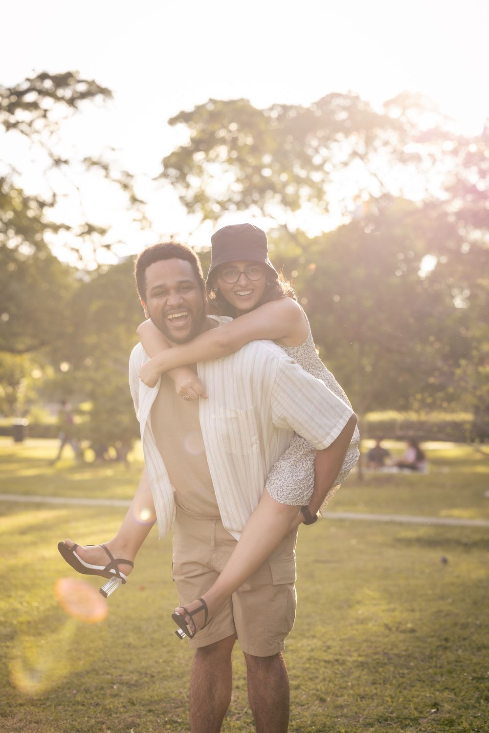 Two people sharing a piggyback ride and laughing together in a sunny park during golden hour.