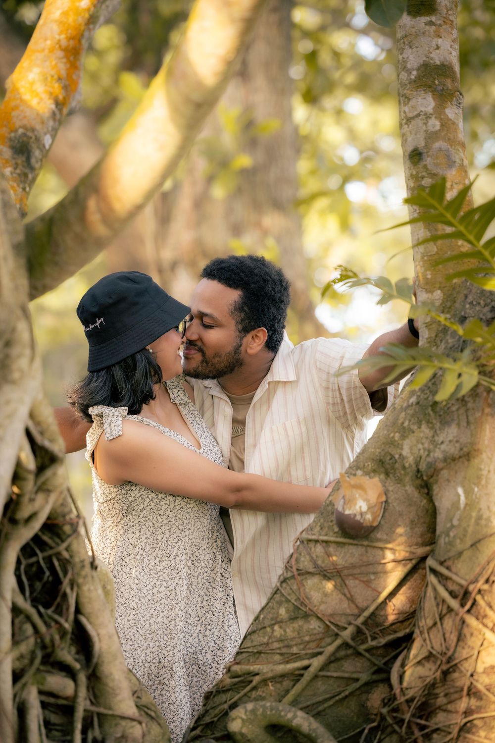 A couple shares a romantic kiss in a sunlit forest setting with golden light filtering through the trees.