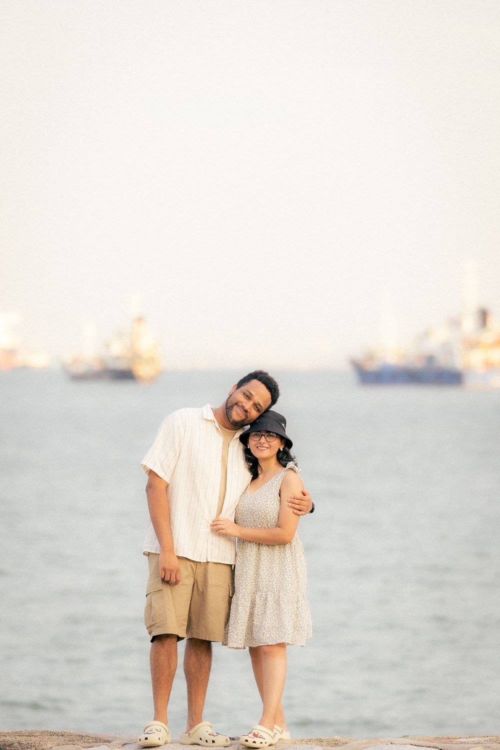 A couple shares a tender moment while walking together on the beach at sunset with ocean waves in the background.