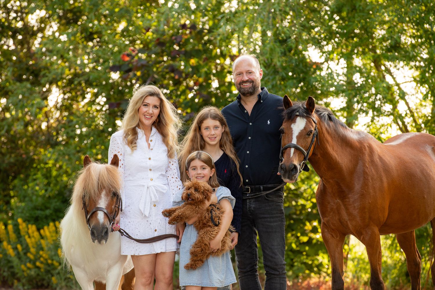 A group poses with horses along a tree-lined path during a sunny autumn day for outdoor photos.