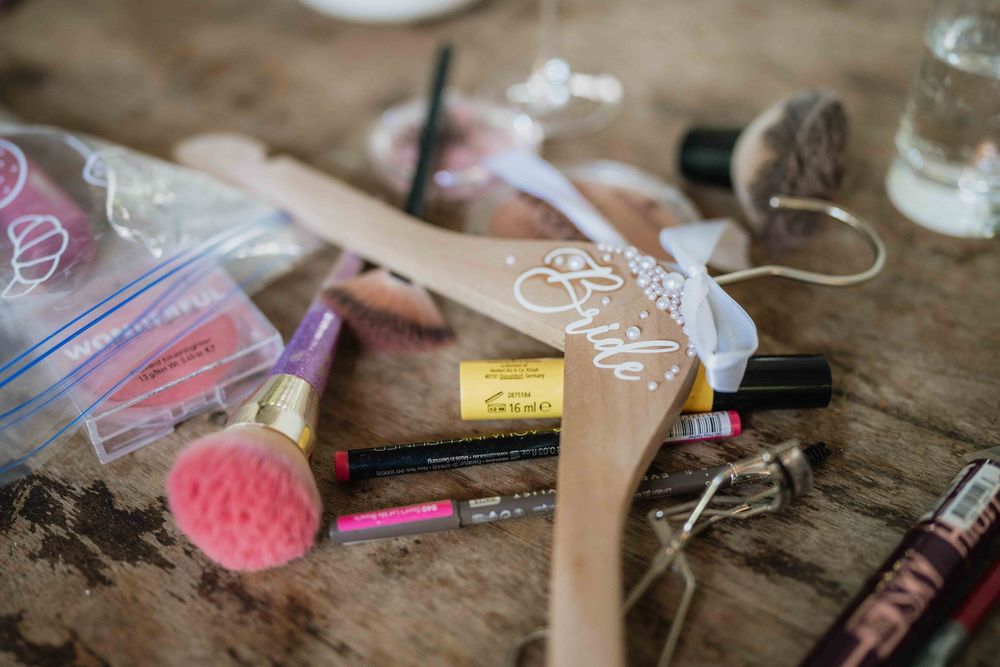 Wedding day preparation supplies and makeup scattered on wooden surface.