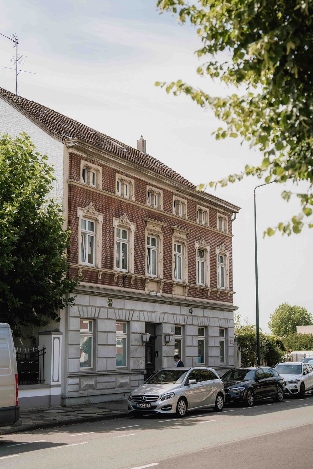 Exterior view of a classic brick building with white trim and parked cars along the street.