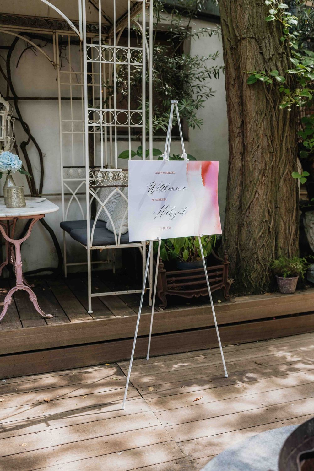 Outdoor wedding setup with hanging signs and wooden deck surrounded by trees.