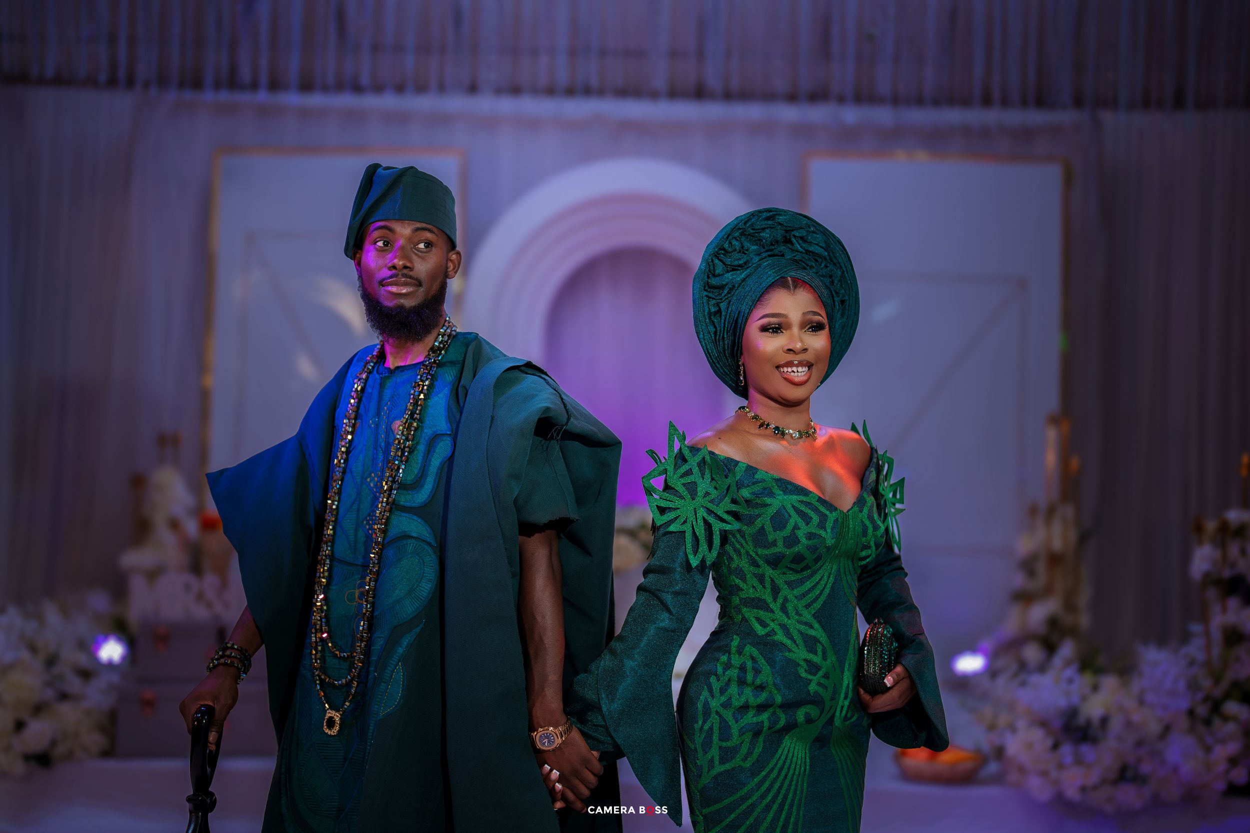 Two people in formal attire at an event with an arched backdrop, one wearing a green sequined gown and the other in blue.