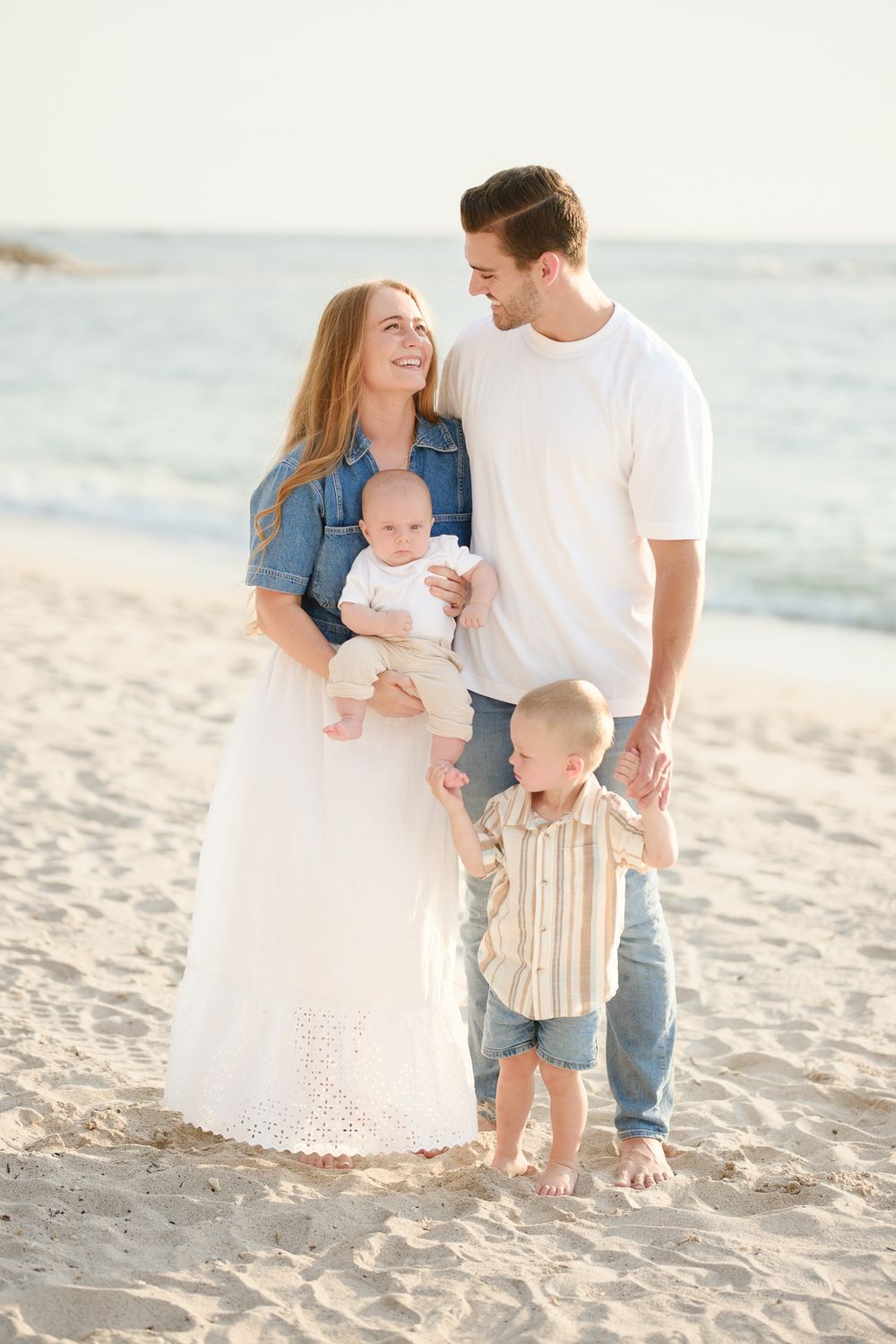 Family having a candid moment together while walking on a sunny beach in light colored outfits.