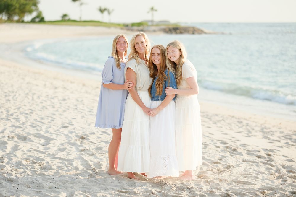A group of people in white dresses pose together while standing on a sunny tropical beach.
