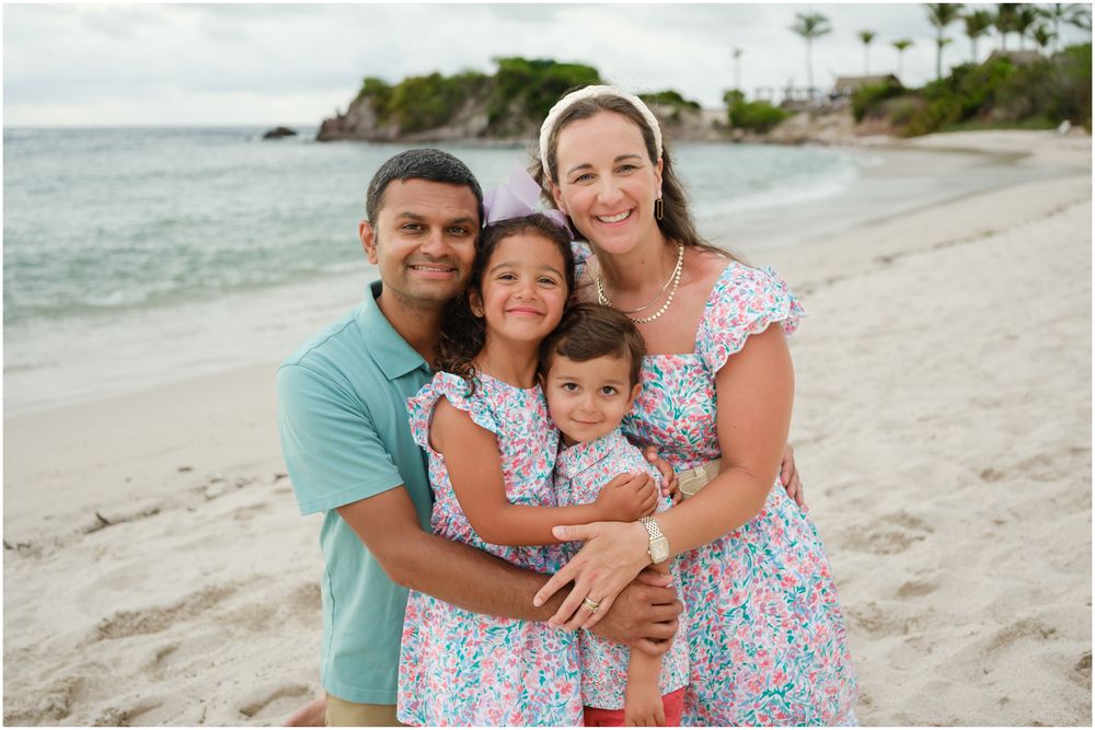 A family shares loving embraces while posing for photos together on a sunny beach.