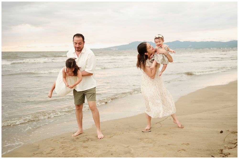 A family enjoys playful moments together on a sandy beach with ocean waves and mountains in the background.