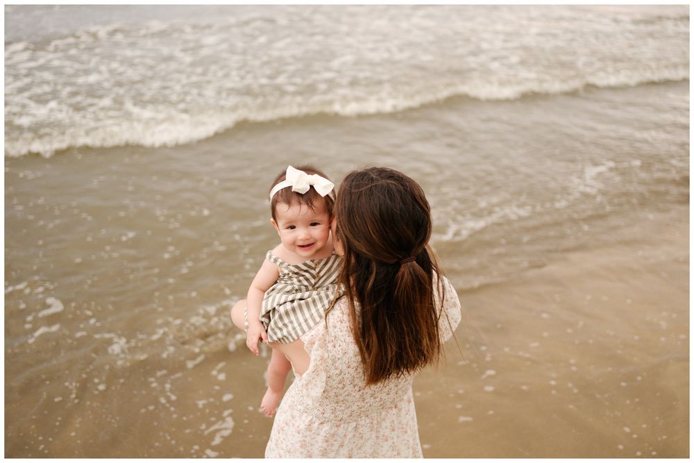 Parent and baby share an intimate moment at the edge of the ocean surf.