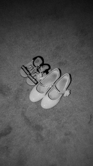 Black and white photograph of two pairs of light-colored ballet or tap dance shoes arranged on a dark floor.
