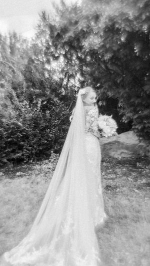 A black and white photograph shows an ethereal wedding scene with a flowing white dress and veil against a garden backdrop.