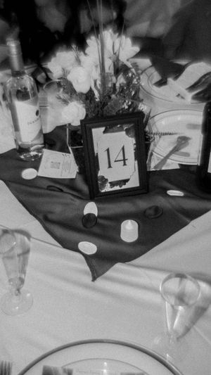 A black and white table setting with a framed number 14, floral centerpiece, glassware, and candles on a white tablecloth.