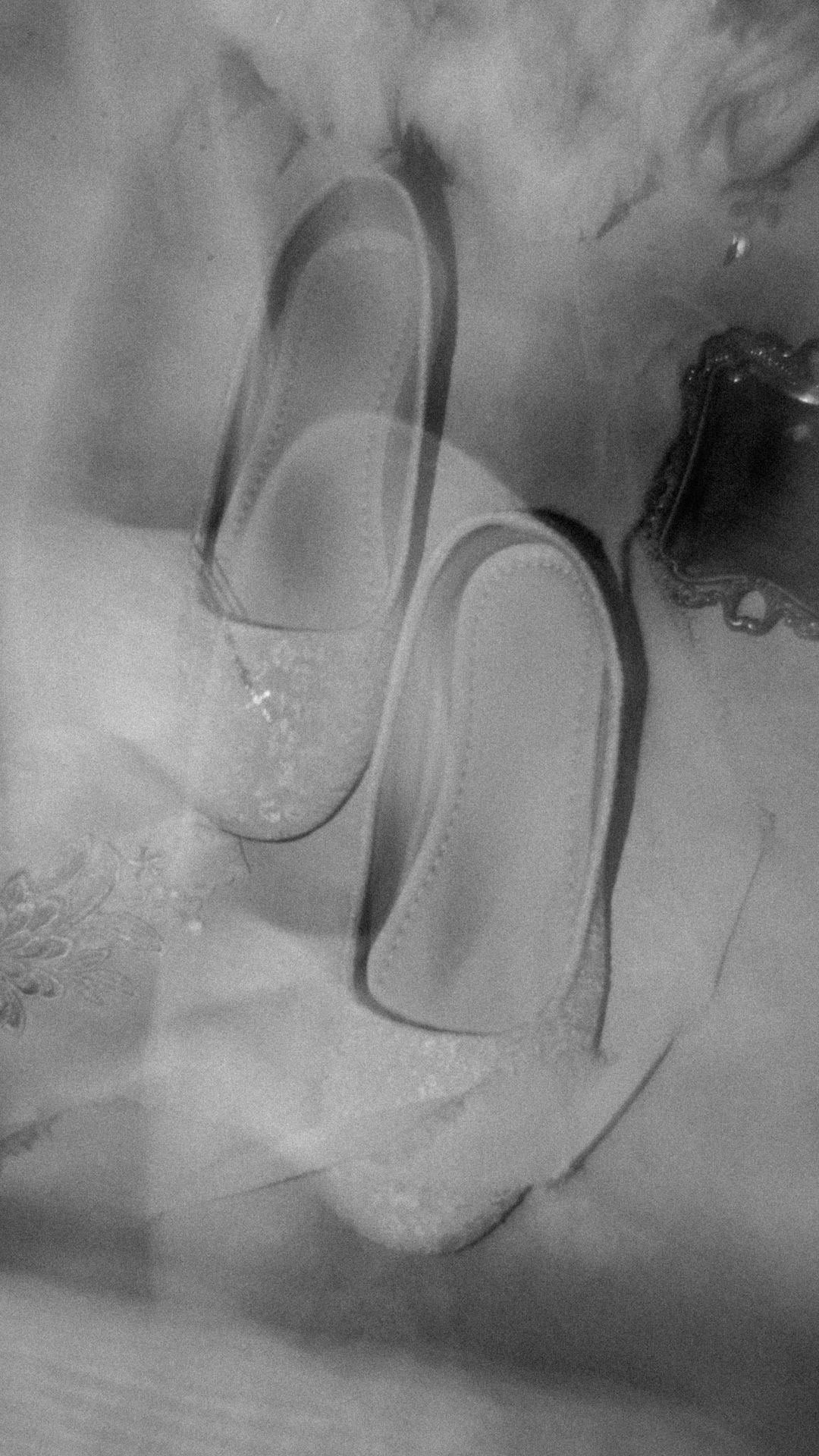 A black and white artistic photograph of ballet flats casting shadows on a misty or smoky surface.