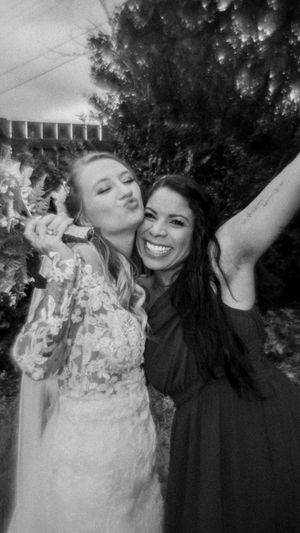 A bride and another person playfully smash cake into each other's faces during a celebration outdoors.