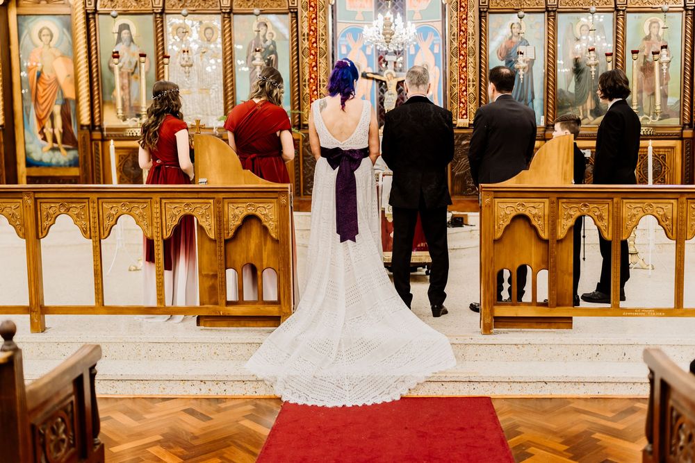A wedding ceremony in a traditional church with a cathedral veil trailing on red carpet in front of ornate altar panels.