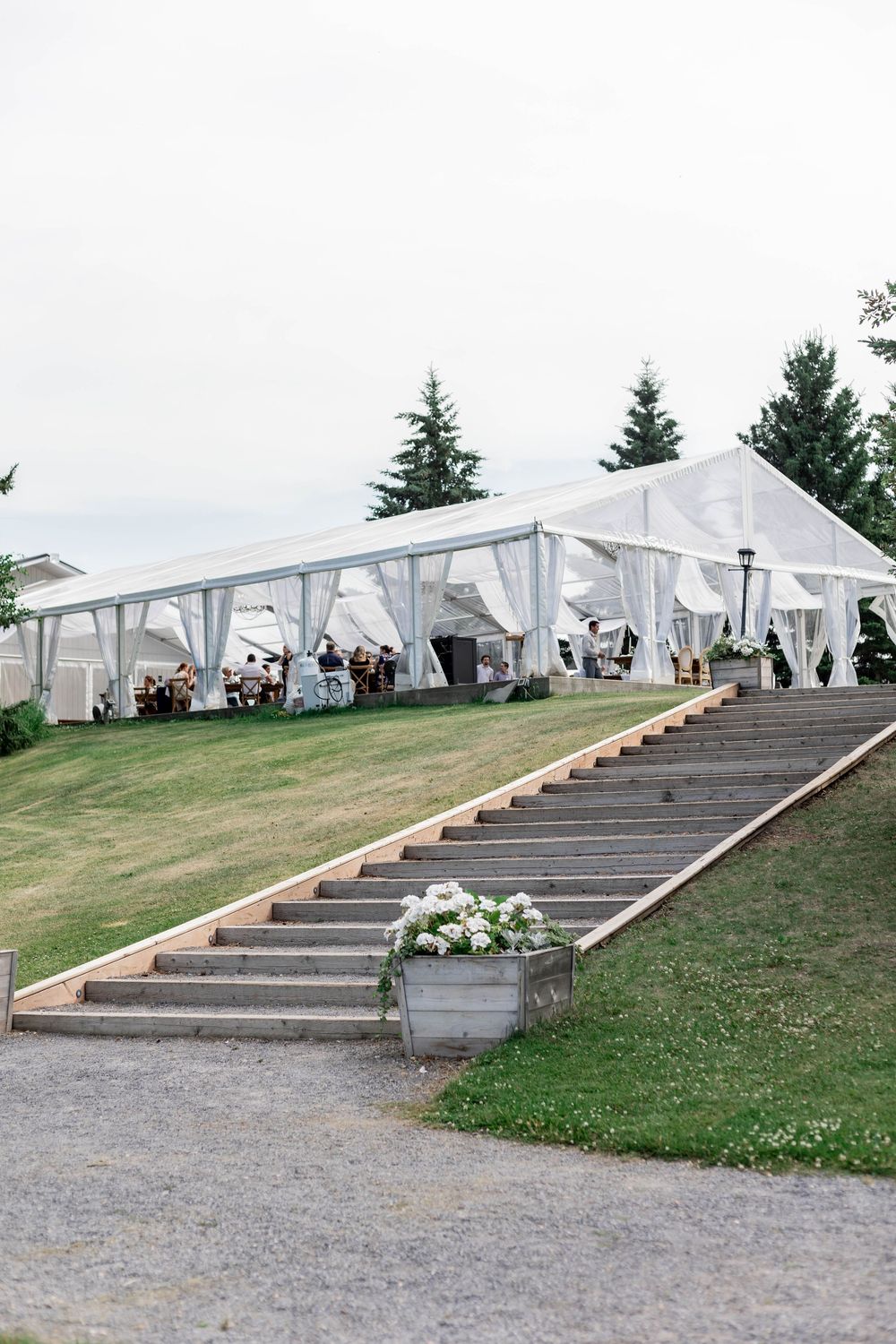 White event tents set up along a stepped landscape with stone stairs leading up a grassy hillside.