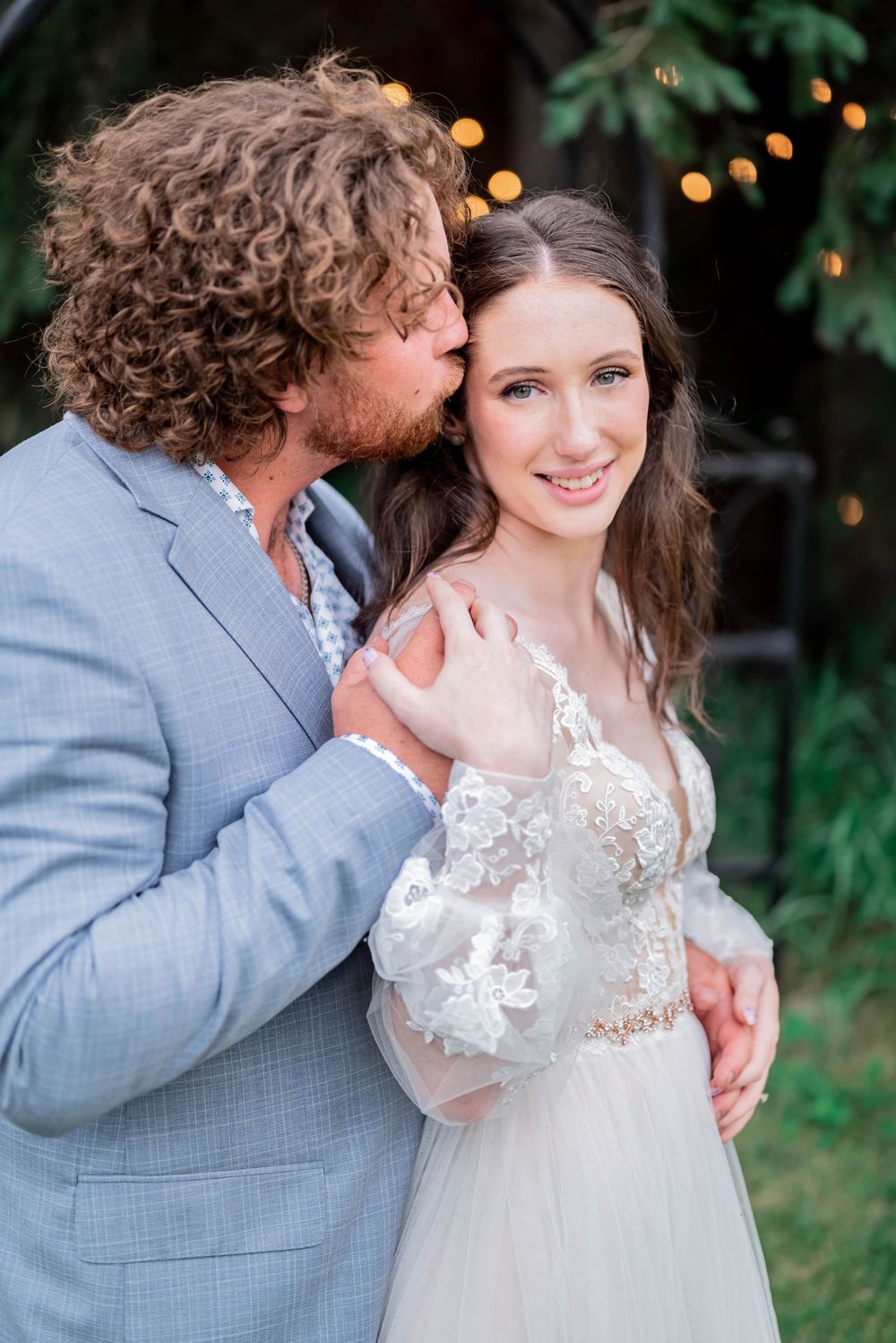 A romantic outdoor wedding photoshoot showing an intimate moment between a couple in gray suit and white lace dress.