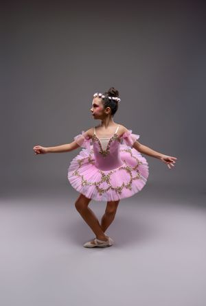 Young ballerina in pink tutu and floral headpiece performs graceful ballet pose in studio.