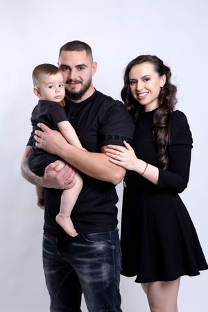 Family wearing coordinated black outfits poses together for a studio portrait against white background.