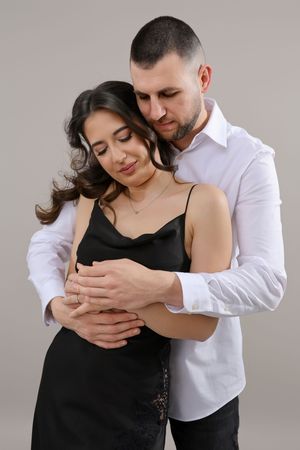 A man in a white shirt tenderly embraces a woman in a black dress, both posing for a romantic couple portrait.
