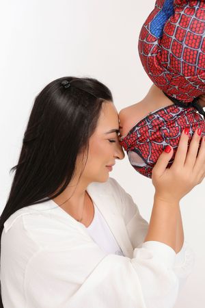 A woman in a white robe affectionately nuzzles a child dressed in a Spider-Man costume against a white background.