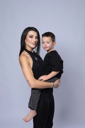 Studio family photoshoot with matching black outfits against light gray background.