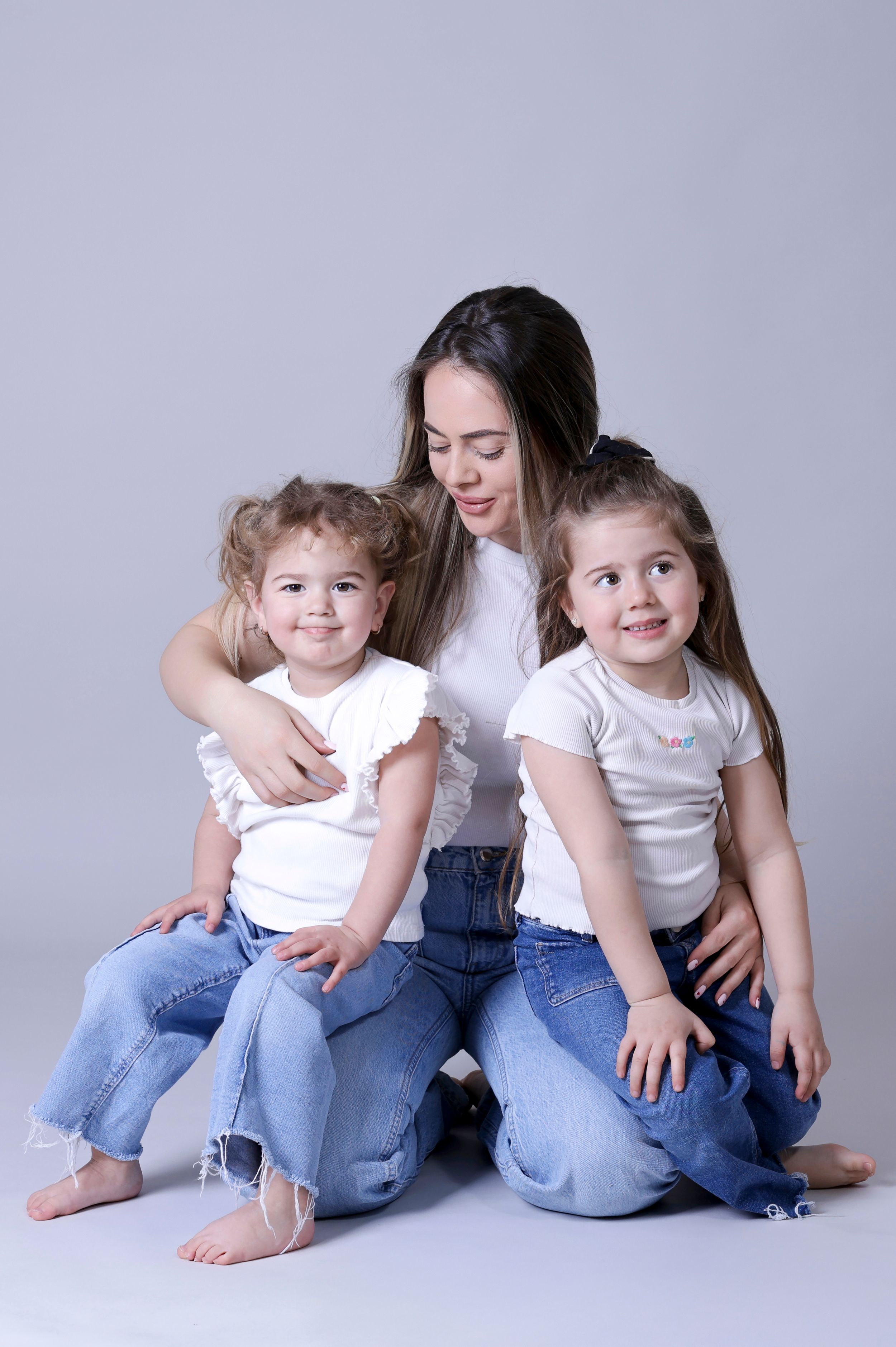 Casual family portrait with everyone wearing jeans and sitting together on white background.
