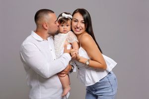 Family portrait in coordinated white outfits embracing against grey studio backdrop.