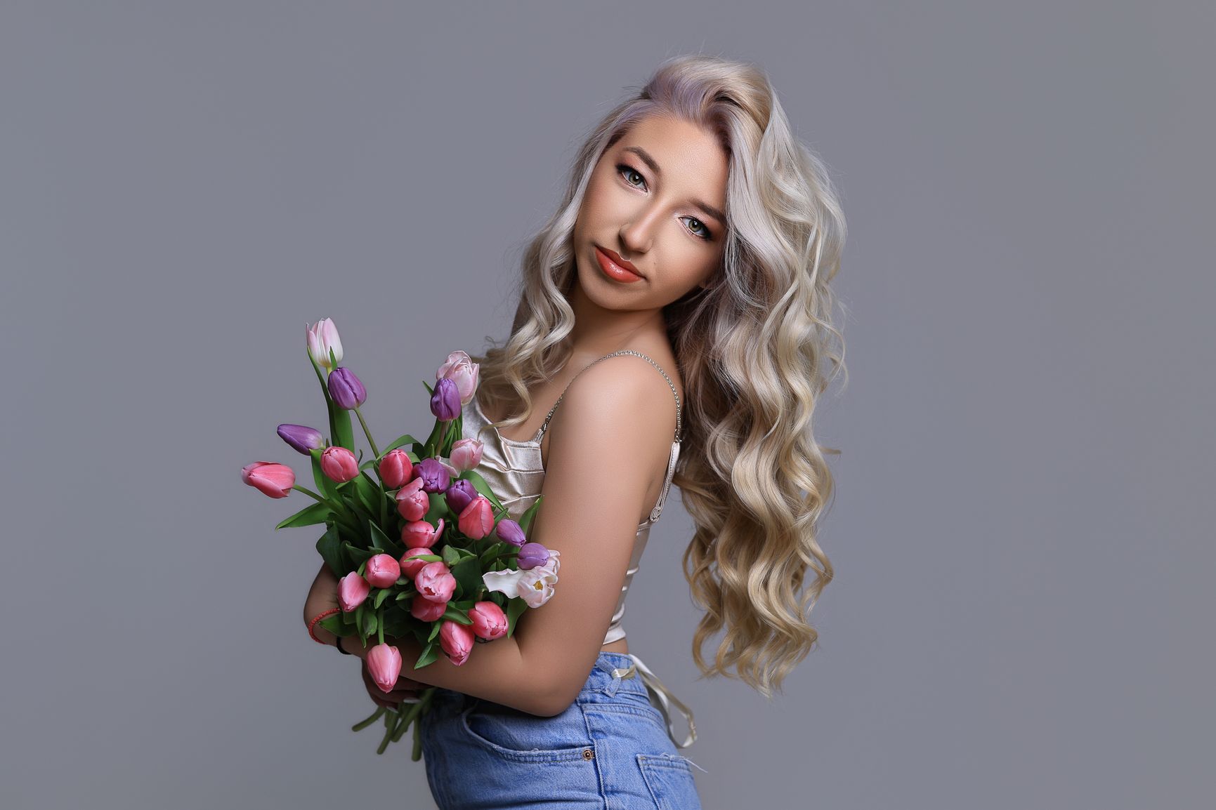 Glamour portrait with pink tulips and elegant styling against grey studio backdrop.