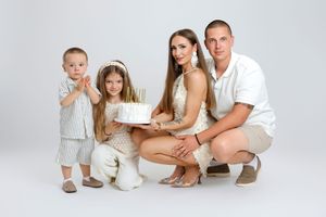 Happy family of four celebrating a birthday with a white cake in a bright studio setting.